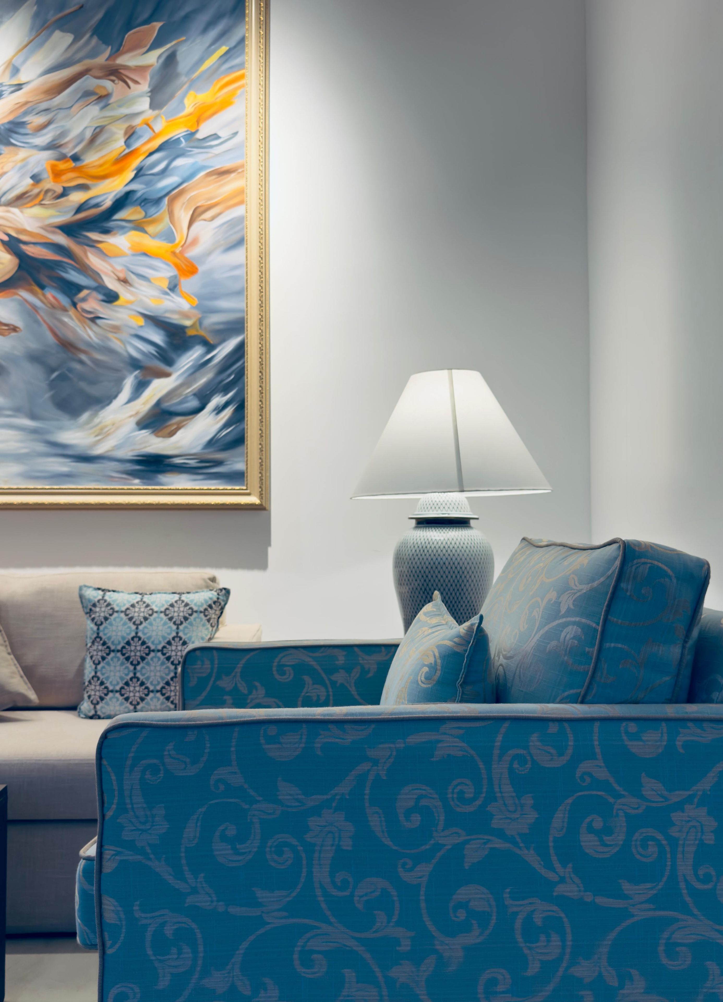 Ein Wohnzimmer mit einer Couch, einer Lampe und einem Gemälde an der Wand.