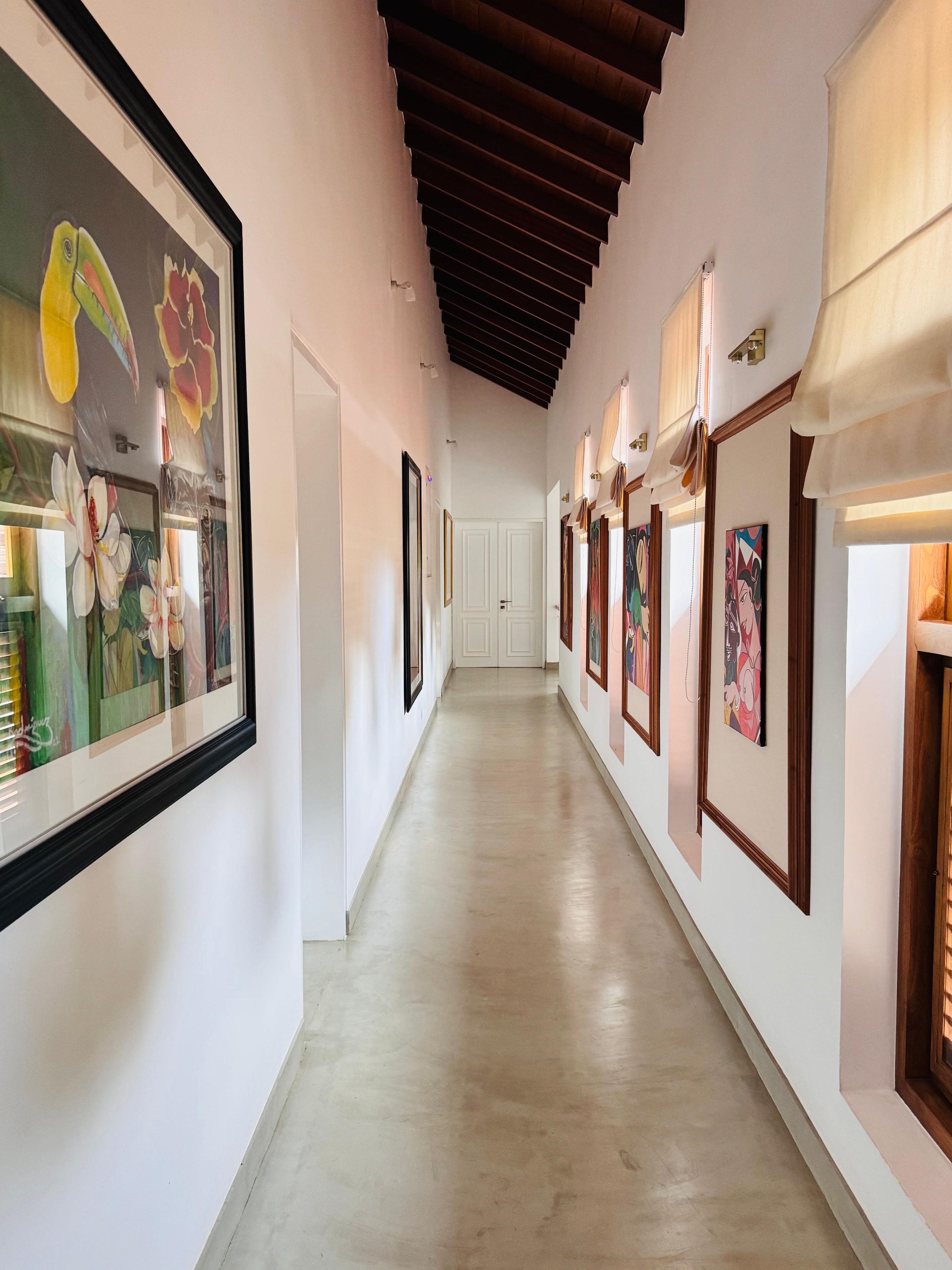 A hallway with framed artwork on the walls, a wooden ceiling, and a door at the end.