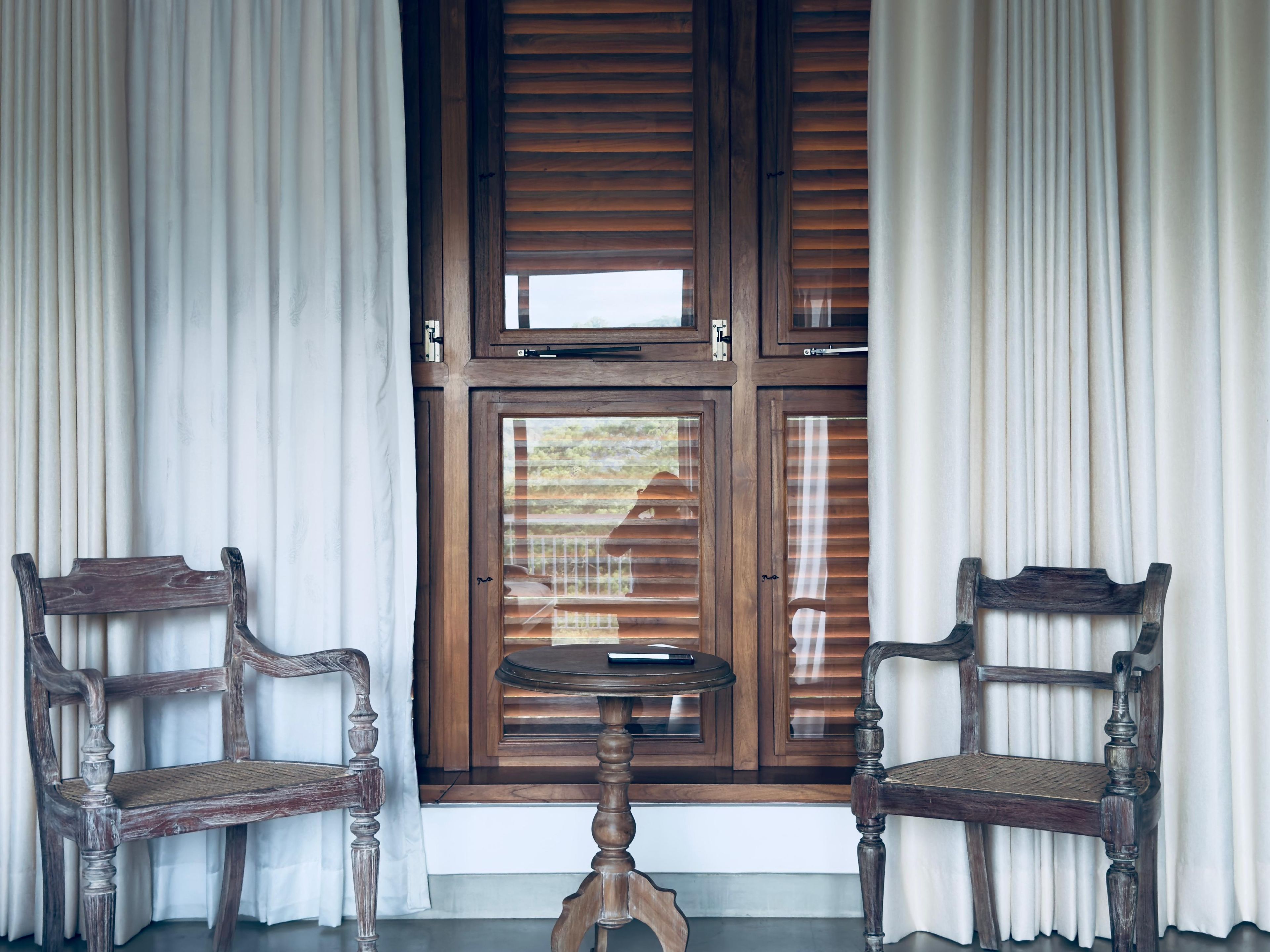 Une pièce avec deux chaises en bois, une petite table et une fenêtre avec des volets en bois.