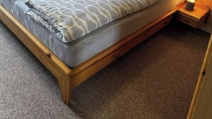 A double bed with a wooden frame and grey bedding, a stone wall, and framed pictures on the wall. - Hex"nhausla in Aufsess (Aufsess)