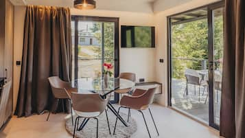 Un comedor moderno con una mesa y sillas de vidrio, una alfombra redonda y vistas a un jardín a través de puertas correderas grandes.