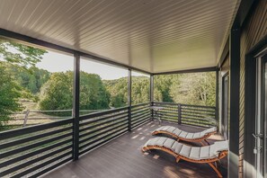 A covered balcony with two lounge chairs, a table, and a view of a forested area. - Luxury Forest Retreat With Pool Access (Karlovac)