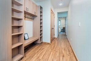 Un pasillo con piso de madera, un armario empotrado con estantes y perchero, y una puerta que da a otra habitación.