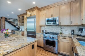 A modern kitchen with wooden cabinets, stainless steel appliances, granite countertops, and a built-in oven.