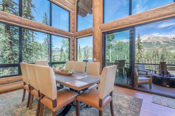 A wooden interior with a dining table and chairs, large windows offering mountain views.