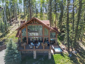 Une cabane en rondins dotée d’une grande façade vitrée, d’un espace extérieur aménagé pour s’asseoir et d’un jacuzzi.