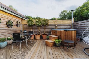 Eine Holzterrasse mit Whirlpool, Tisch und Stühlen sowie Blumentöpfen.