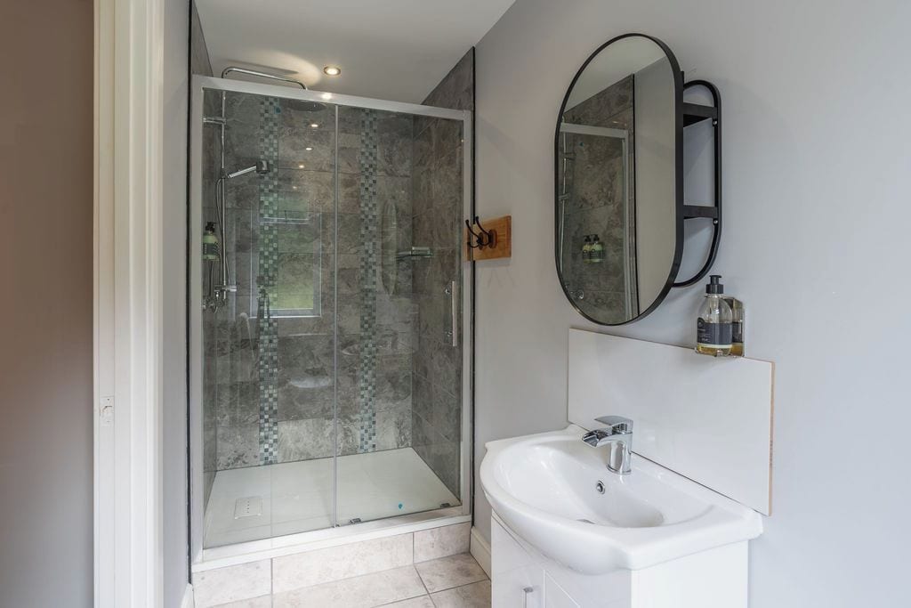 A modern bathroom with a glass-enclosed shower, a white sink, and a large mirror.