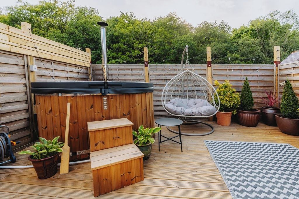 Eine Holzterrasse mit Whirlpool, einer Hängematte und Topfpflanzen.