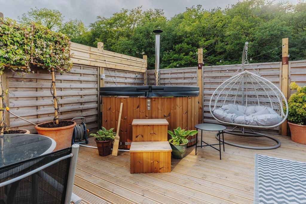 A wooden deck with a hot tub, a hanging chair, and potted plants.