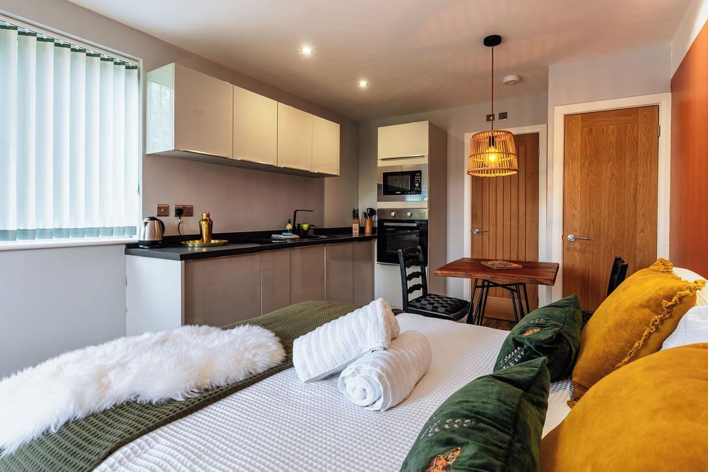 Una habitación de hotel pequeña con kitchenette, una cama con una manta blanca mullida y una mesa de comedor.