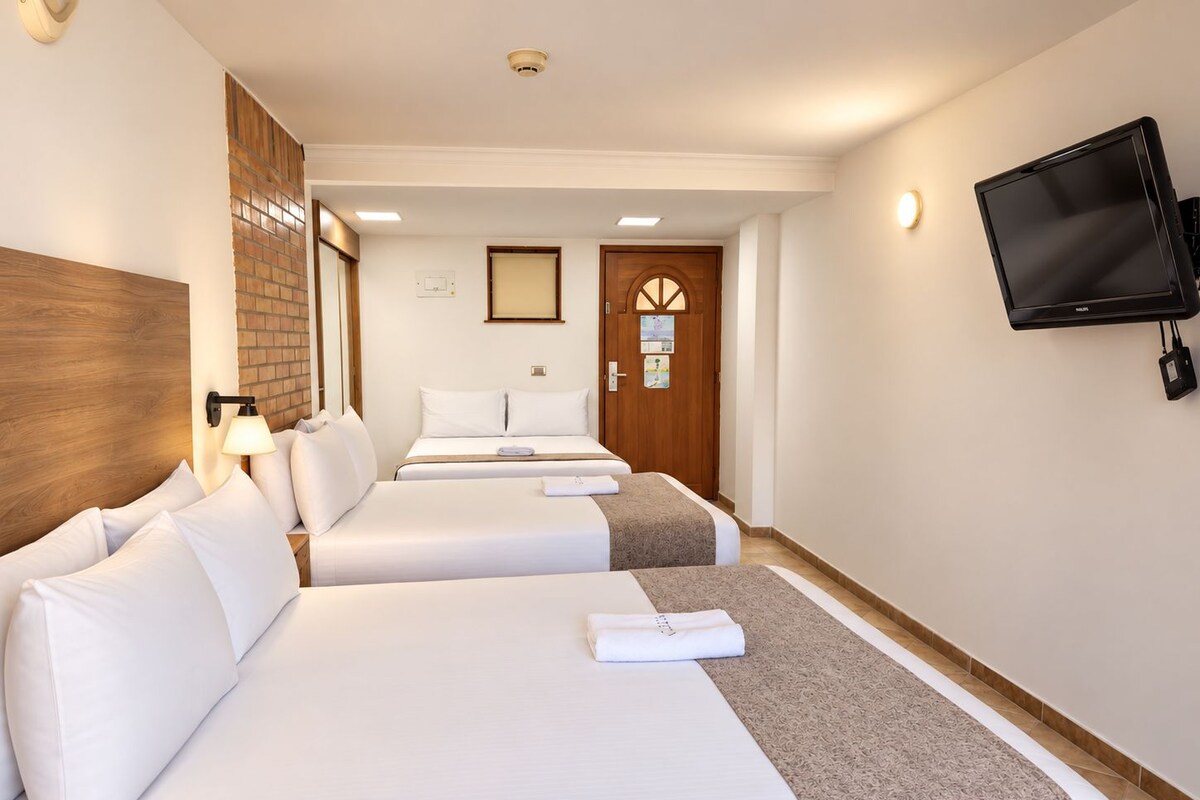 A hotel room with two beds, a TV mounted on the wall, and a door with a window.