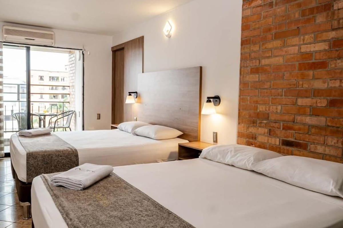 Habitació d'hotel amb dos llits, una paret de maó i vista cap a l'exterior.