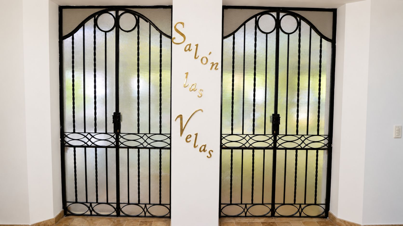 Un juego de puertas dobles con un diseño metálico decorativo y un letrero que dice 'Salón las Velas'.