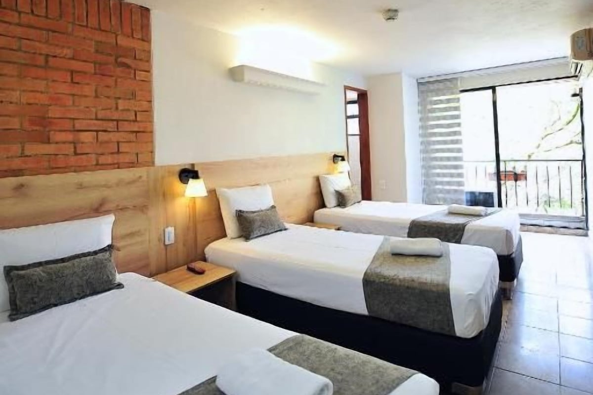 Habitació d'hotel amb dos llits, una paret decorativa de maó, una finestra amb persianes i un balcó.