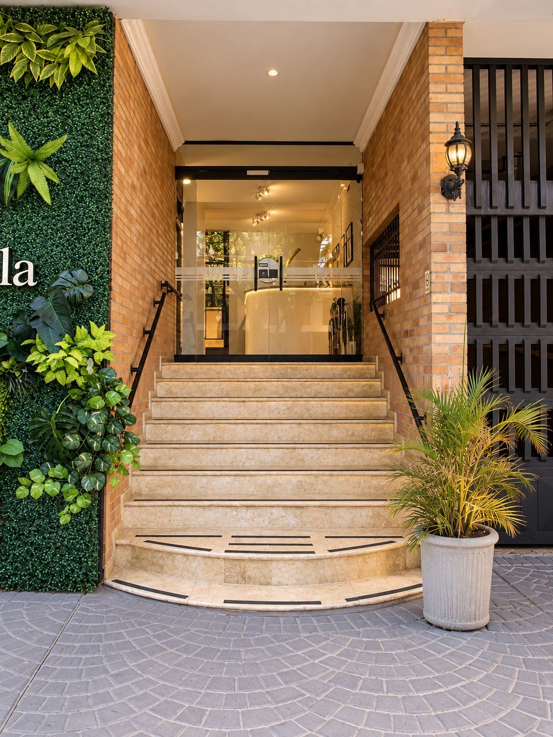 Un escalier menant à un espace d’accueil avec une porte en verre, une plante en pot et un mur recouvert de verdure.