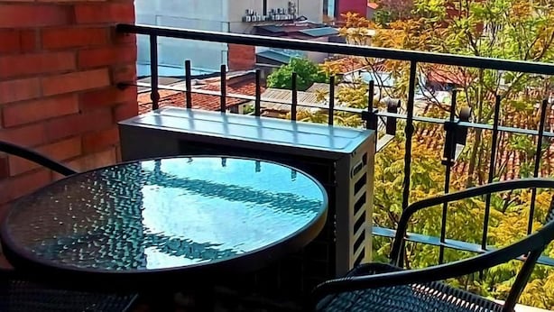 Ein Balkon mit Glastisch und Stühlen, mit Blick auf eine Stadtlandschaft aus Gebäuden und Bäumen.