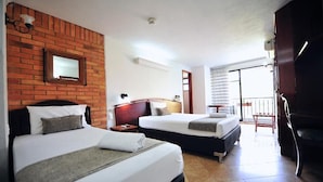 Ein Hotelzimmer mit zwei Betten, einer Wand aus Ziegelsteinen, einem kleinen Fenster und einem Balkon.