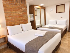 A hotel room with two beds, a brick wall, a wooden wardrobe, and a small desk with a lamp. - CV hotel medellin  (Medellin)