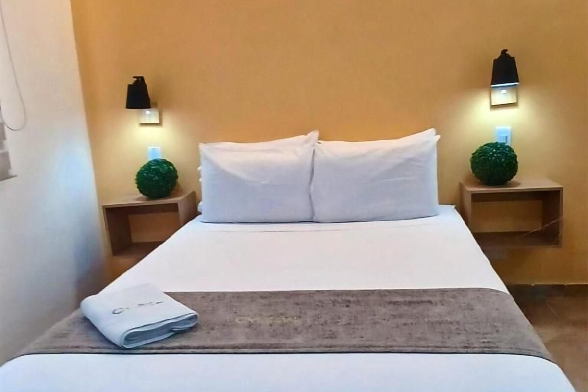Habitació d'hotel amb llit, dues tauletes de nit, una làmpada i una planta petita en test.