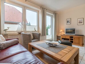 Un salon confortable avec un canapé, une table basse, un téléviseur et une fenêtre avec des rideaux.