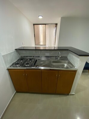A compact kitchen with a gas stove, a sink, and wooden cabinets. - Private apartment ideal for working, Downtown Medellín (Medellín)