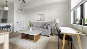 A modern living room with a sofa, coffee table, and a desk with a chair. There is a window with blinds, a lamp, and a plant on the coffee table. - Landing Incredible 1bd, Gym, Clubhouse (North Fort Myers)