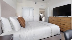A hotel room with a bed, a television, a dresser, and a door leading to a kitchenette. - Landing Incredible 1bd, Gym, Clubhouse (North Fort Myers)