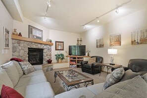 A living room with a stone fireplace, a television, and a fireplace mantel with decorative items. - Creekside Frisco Retreat 4 Private Suites, Pool & Hot Tubs (Frisco)