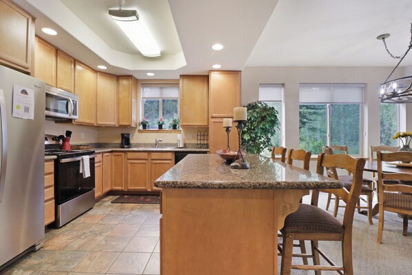 A modern kitchen with granite countertops, wooden cabinets, and a central island with seating. - Creekside Frisco Retreat 4 Private Suites, Pool & Hot Tubs (Frisco)