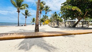 A beach with palm trees, a wooden deck, and sun loungers. - Born | 2-bedroom modern apartment with pools (Bávaro)