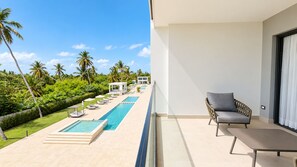 A balcony with a pool, lounge chairs, and a view of a tropical landscape. - Born | 2-bedroom modern apartment with pools (Bávaro)