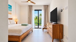 A hotel room with a bed, a TV on a wooden dresser, a ceiling fan, and a view of palm trees through a glass door. - Born | 2-bedroom modern apartment with pools (Bávaro)
