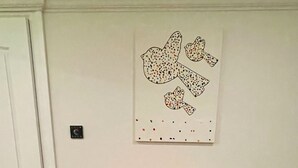 Huoneessa on puulattia, valkoinen ovi, vaaleanpunainen pöytä sekä kaksi tuolia, joiden selkänojat ovat sinisiä ja keltaisia.