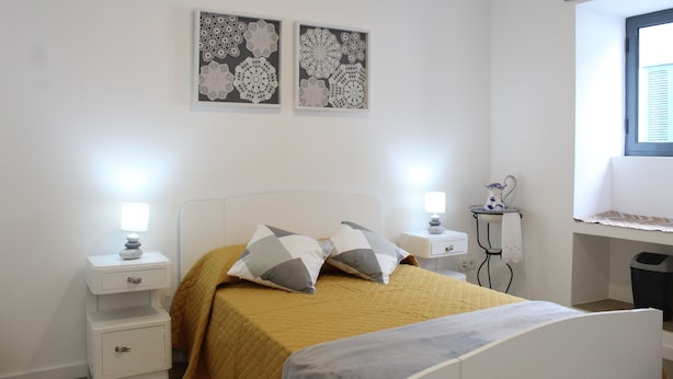 A bedroom with a bed, two bedside tables, a nightstand, a desk, and a window with blinds. - Cantinho do Calhau (Lagoa)