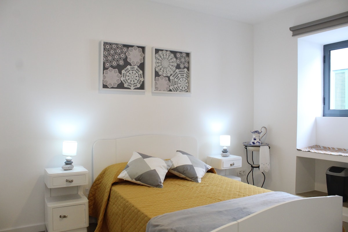 Ein Schlafzimmer mit einem Bett, zwei Nachttischen, einem Schreibtisch und einem Fenster mit Jalousien.