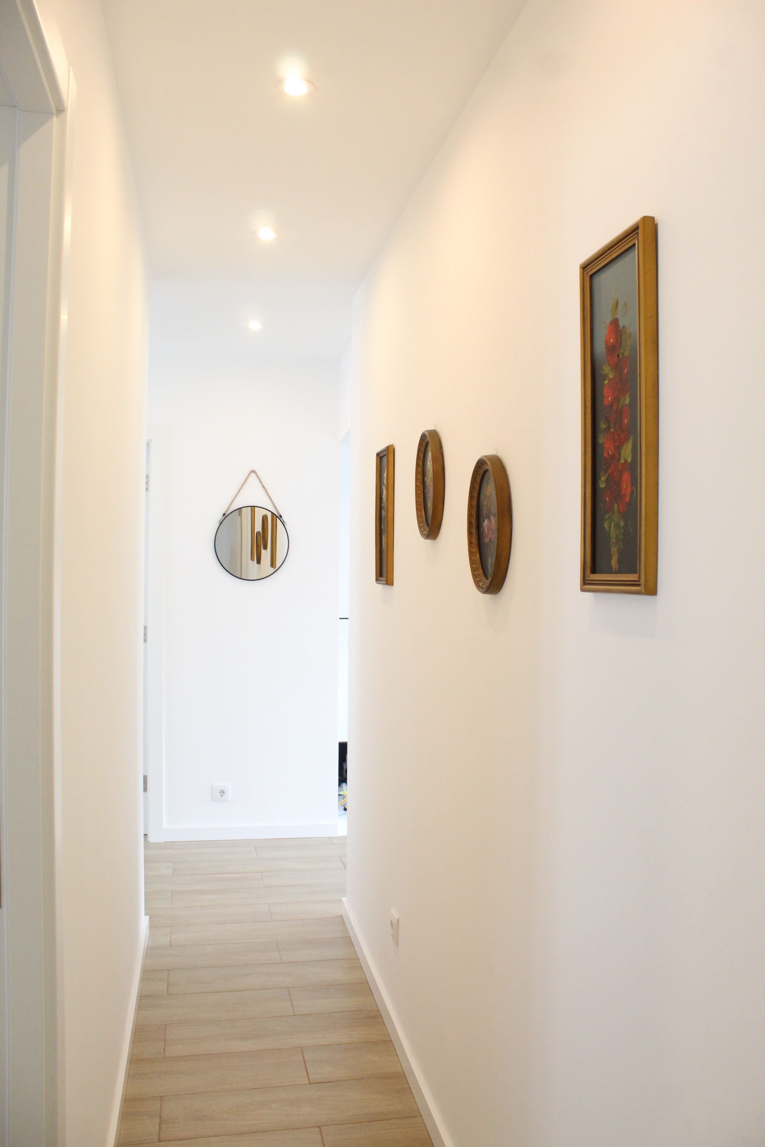 Un pasillo con piso de madera, paredes blancas y una puerta al final.