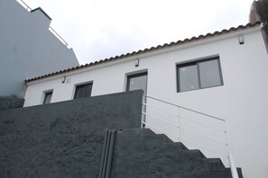 Un edificio con fachada blanca, techo de tejas rojas y una escalera que lleva a la entrada.