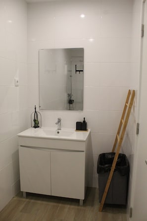 Ein Badezimmer mit einem weißen Waschtisch, einem Spiegel, einer Dusche und einer Holzleiter, die an der Wand lehnt.