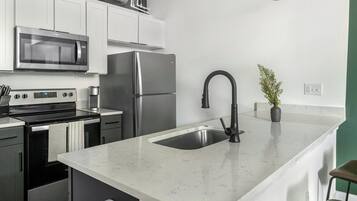 A modern kitchen with stainless steel appliances, a marble countertop, and a black faucet.