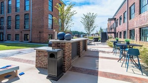 Un área de patio al aire libre con edificios de ladrillo, mobiliario exterior y una parrilla.