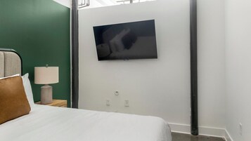 A hotel room with a bed, a nightstand with a lamp, a TV mounted on the wall, and a green accent wall.