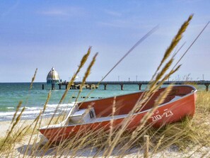 A beach with a red boat, a pier, and a dome structure in the background. - Holiday Home in Zingst With Swimming Pool (Zingst)