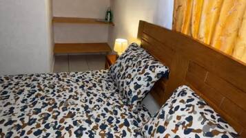 Un dormitorio con cama, mesita de noche, lámpara colgante y ventana con cortinas.