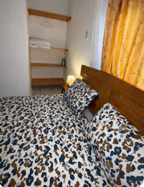 A bedroom with a bed, a nightstand, a hanging light, and a window with curtains. - Ideal apartment with bedroom, living room, kitchen, and shower (louis)