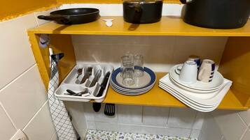 Cocina compacta con estufa a gas, un lavamanos pequeño y un estante amarillo con utensilios de cocina y vajilla.