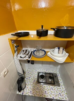 A compact kitchen with a gas stove, a small sink, and a yellow shelf with cookware and dishes. - Ideal apartment with bedroom, living room, kitchen, and shower (louis)