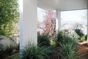 A covered outdoor area with plants and a view of a tree with pink blossoms. - River Views & City Delights (Trevallyn)