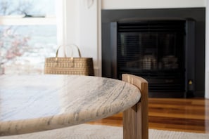 A wooden chair with a curved backrest, a round table with a textured surface, and a fireplace with a black screen in the background. - River Views & City Delights (Trevallyn)
