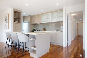 A modern kitchen with a central island, bar stools, and a dining area. - River Views & City Delights (Trevallyn)